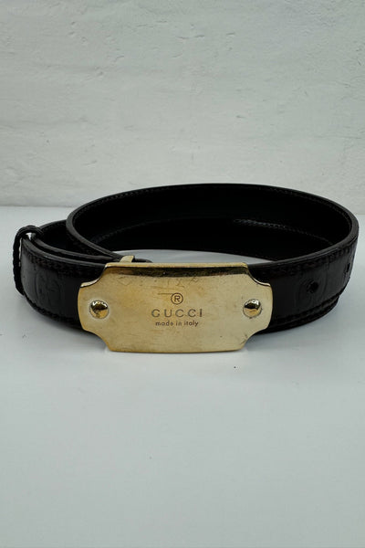 Sort Gucci bælte i glat læder, guldspænde med "GUCCI" og "made in Italy", syninger langs kanten.