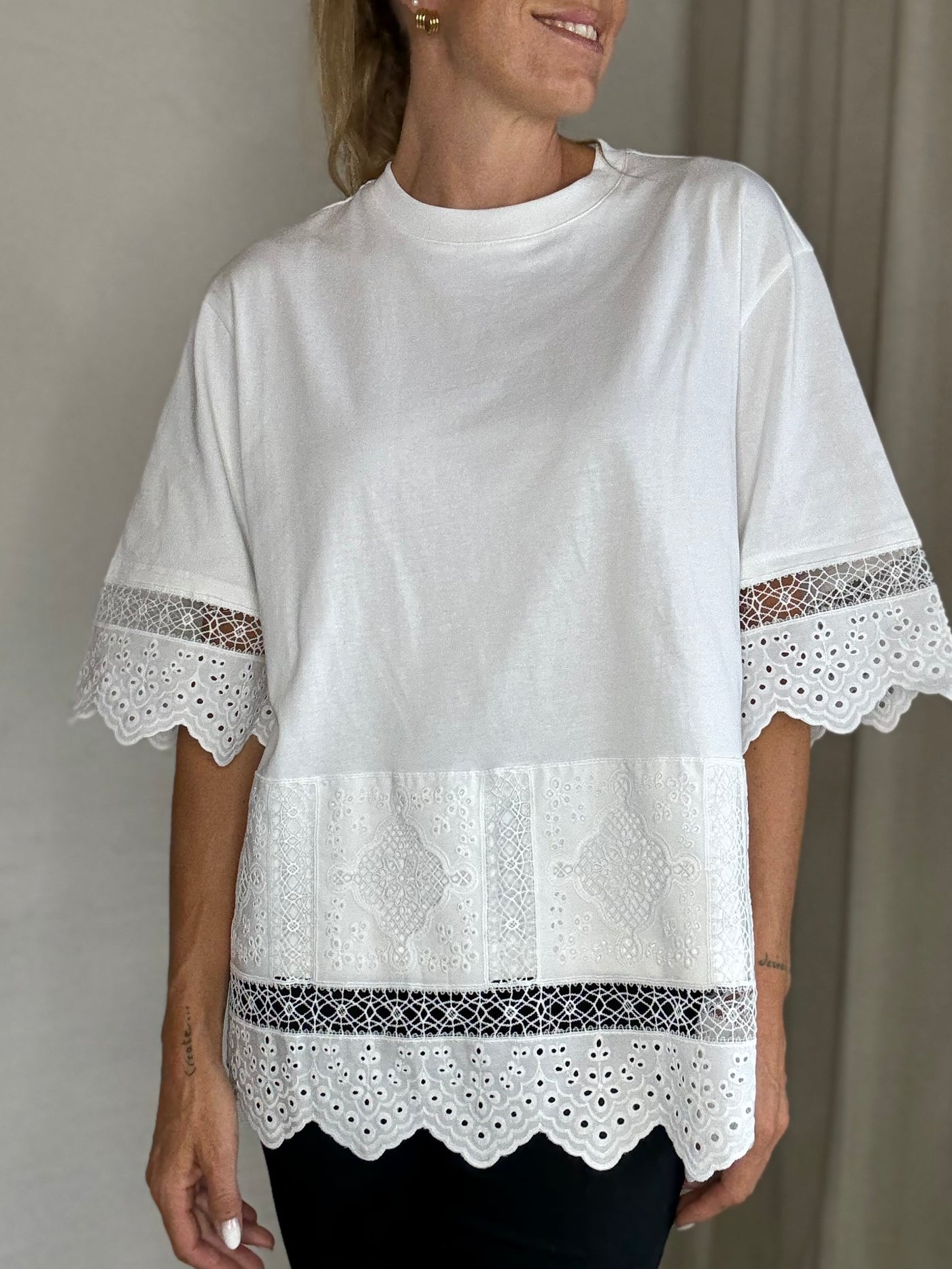 Hvid T-shirt med blonder, afslappet pasform, brede ærmer, bølget kant og dekorative detaljer.