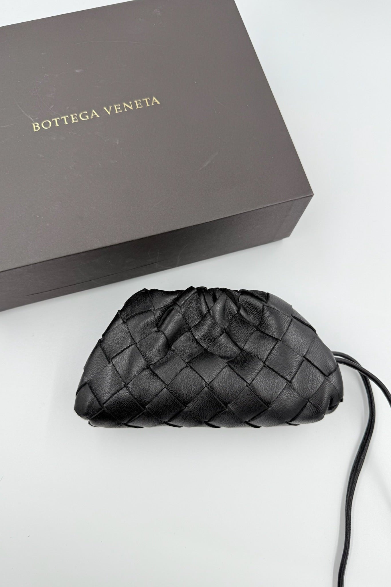 Sort vævet Bottega Veneta taske med skulderrem foran en brun mærket æske.