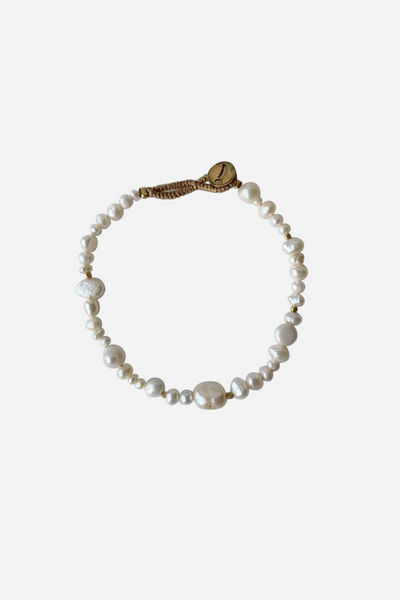 Armbånd med hvide, uregelmæssige perler, guldfarvede afstandsstykker og vævet lukning med knap.