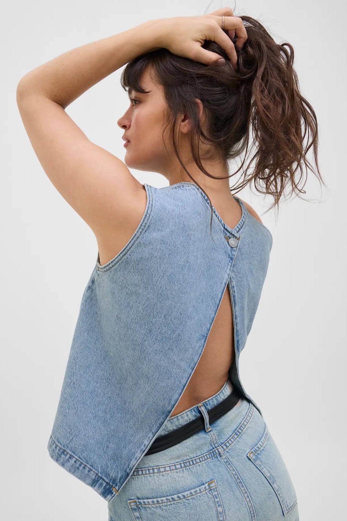 Kvinde i lyseblå top med V-udskæring på ryg, håret oppe, iført lyseblå jeans.